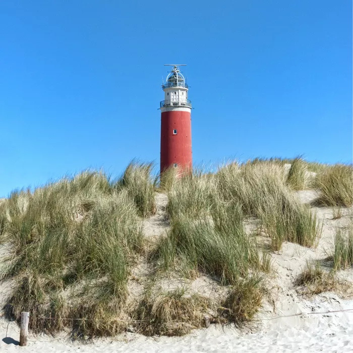 Rode vuurtoren boven een duin met helmgras onder een strakblauwe lucht