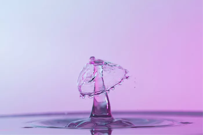 Waterzuil met een schuin gekanteld waterscherm na de botsing van twee druppels, in roze tinten