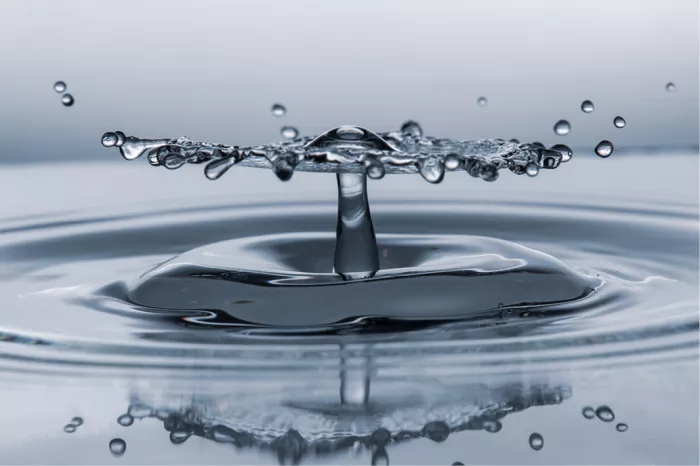Plat waterscherm met druppelrand op een slanke waterzuil, met reflectie in blauwgrijze tinten