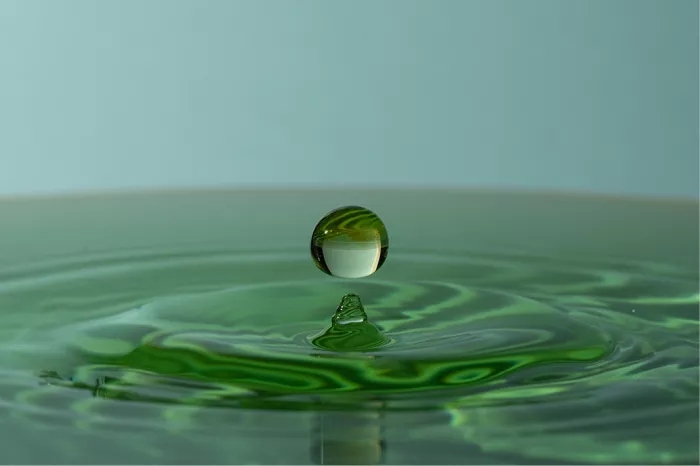 Waterdruppel boven een klein waterpiekje met groene kringen, in blauwgroene tinten