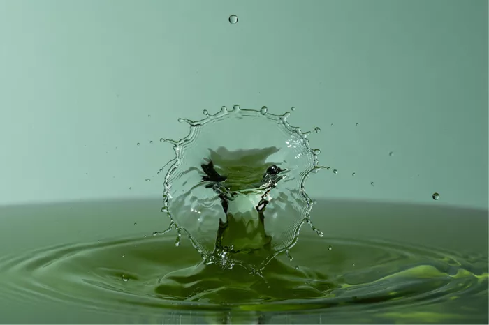 Rond kroonvormig waterscherm rond een groene waterzuil, met een zwevende druppel erboven