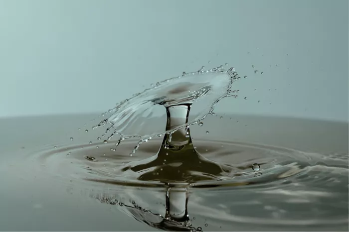 Schuin waterscherm op een korte zuil met reflectie in donker water, in grijze tinten