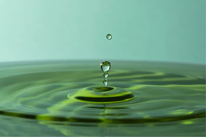 Opspringende waterdruppels boven geelgroene kringen in het water, met een zwevende druppel erboven