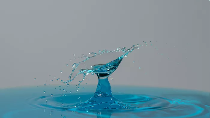 Turquoise waterzuil met een schuin uitwaaierend scherm en spatten, tegen een grijze achtergrond