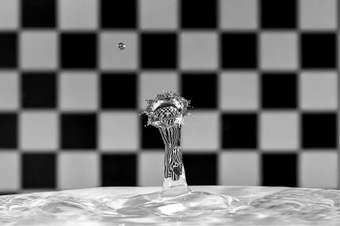 Waterzuil met een kleine kroon bovenaan, met de reflectie van een zwart-wit geblokte achtergrond