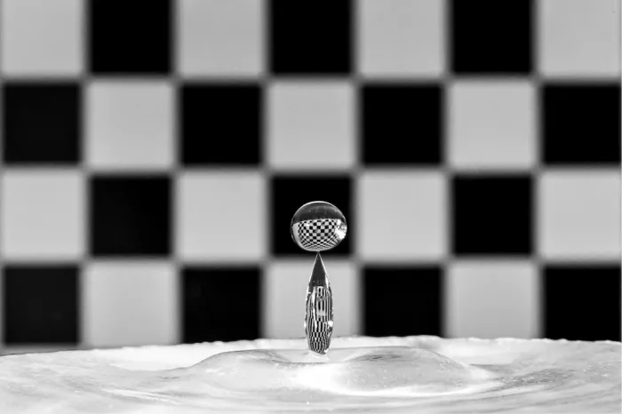 Ronde druppel op een smalle waterzuil met de reflectie van een geblokte achtergrond