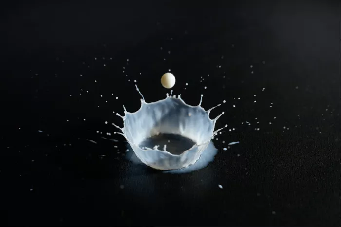 Witte kroon van opspattende melk met een zwevende druppel, op een zwarte ondergrond
