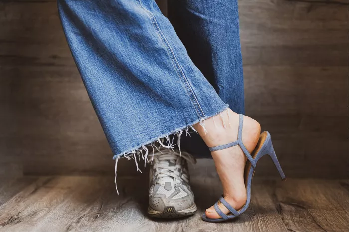 Voeten onder een rafelige jeans, een in een sportschoen en een in een blauwe hakschoen