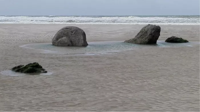 Grote rotsblokken op een nat strand met golven op de achtergrond