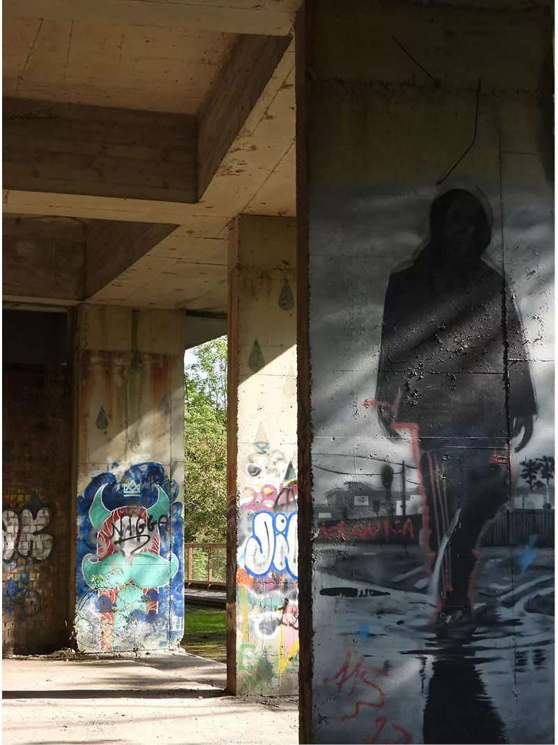 Betonnen pilaren met graffiti en een grote geschilderde figuur in een verlaten gebouw