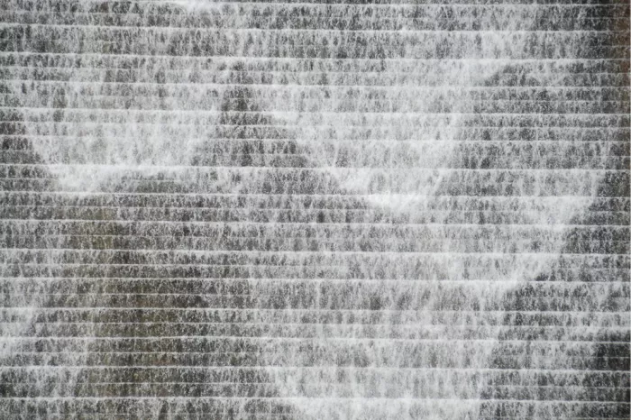 Water stroomt in witte sluiers over een getrapte wand met horizontale lijnen