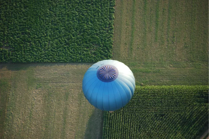 Blauw-witte luchtballon van bovenaf gezien boven groene en bruine akkers
