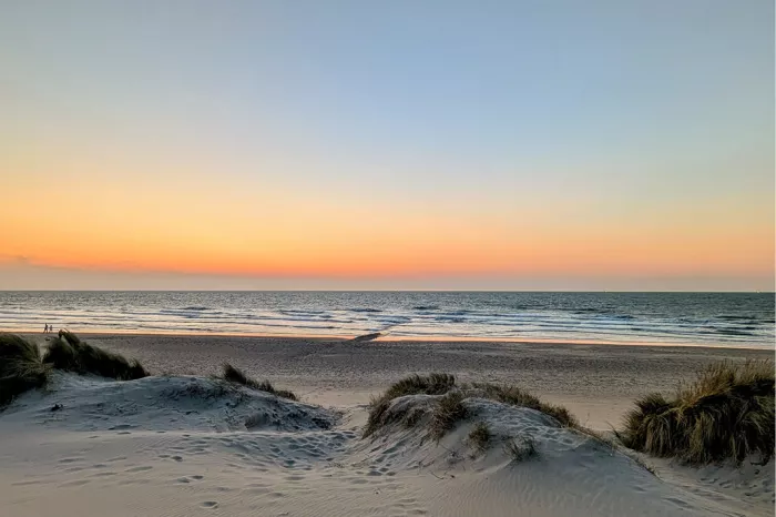 Duinen met helmgras aan zee bij zonsondergang, met een oranje en blauwe lucht