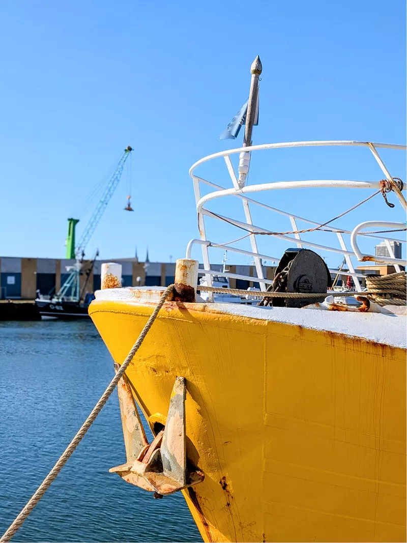 Gele boeg van een vissersboot met anker en touw in een haven onder een blauwe lucht