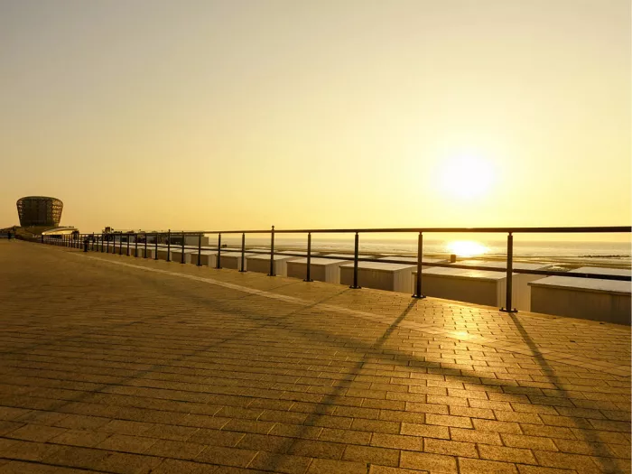 Lange schaduwen van een reling op de dijk bij laagstaande zon, met het casino van Middelkerke