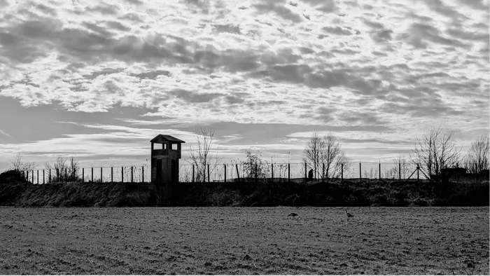 Wachttoren achter een omheining aan het Fort van Breendonk onder een wolkenlucht, in zwart-wit