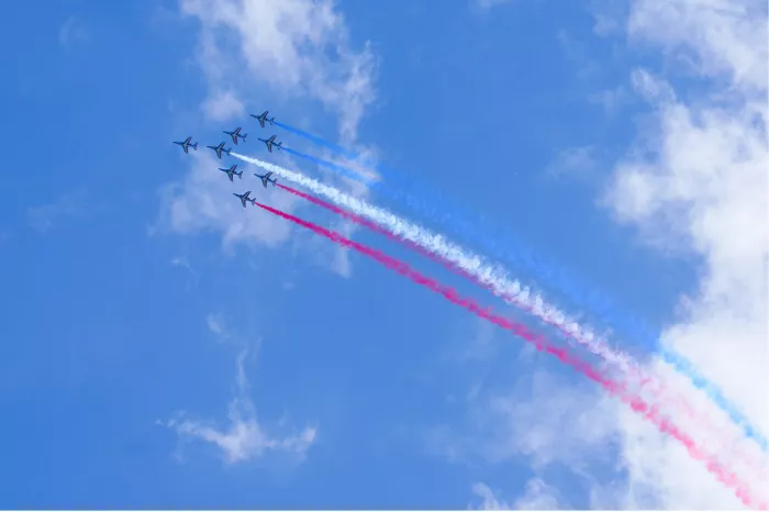 Kleine straaljagers met een boog van roze, witte en blauwe rooksporen in de blauwe lucht