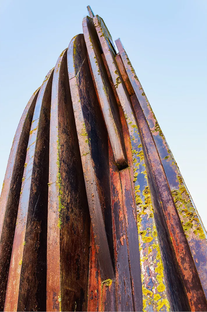 Roestige ijzeren banden van een abstract kunstwerk van onderen gezien tegen een blauwe lucht