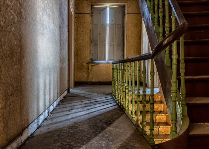 Houten trap met groene spijlen in een oude pastorij, met licht dat door een raam binnenvalt