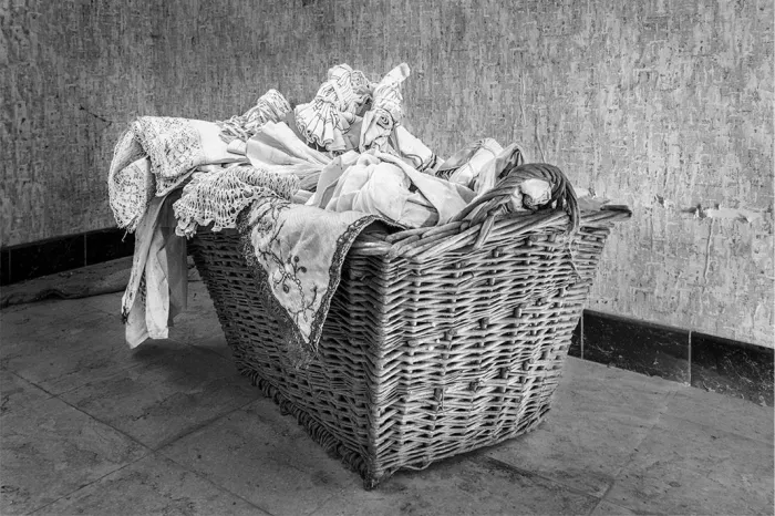 Rieten wasmand vol linnen en kant op een stenen vloer voor een verweerde muur