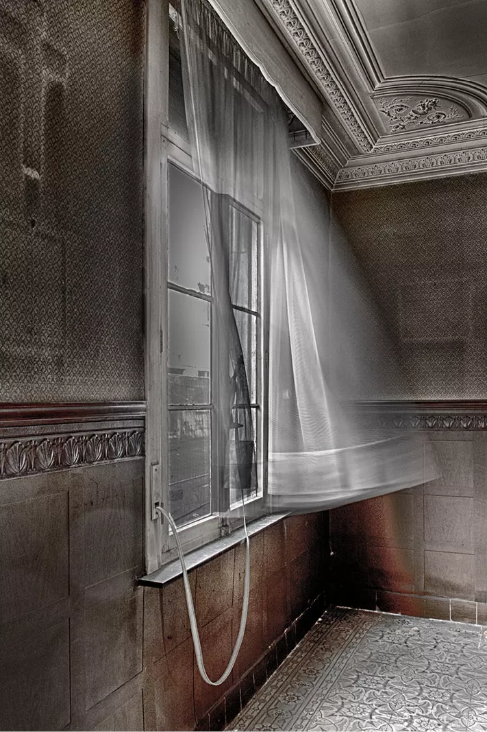 Open raam in een oude kamer met een wapperend wit gordijn dat wazig in beweging is