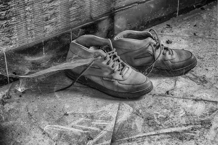 Paar versleten schoenen met spinnenweb op een stoffige tegelvloer