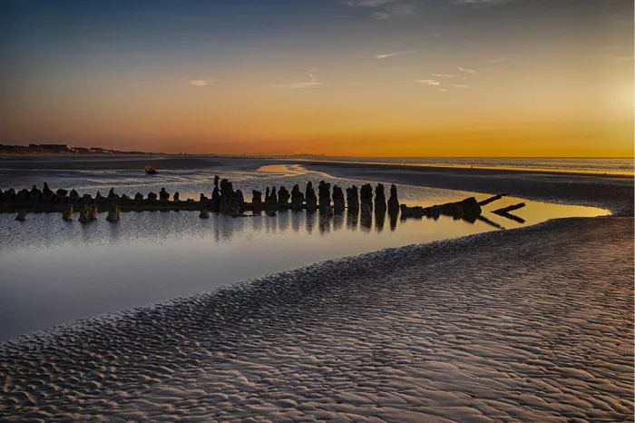 Houten resten van een scheepswrak als silhouet in een plas op het strand bij zonsondergang