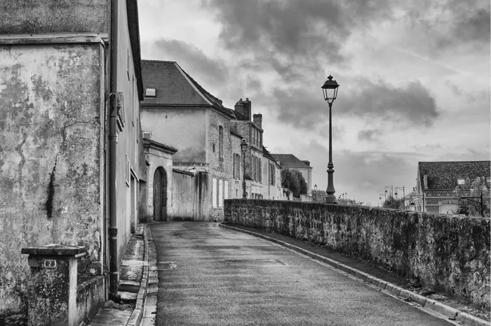 Rustig straatje met oude gevels, een stenen muur en een straatlantaarn onder wolken