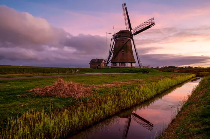Windmolen en huisje aan een sloot onder een roze avondlucht die in het water spiegelt, liggend formaat