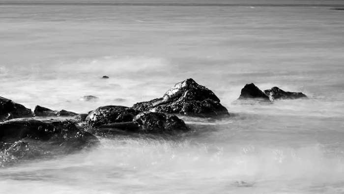 Donkere rotsen in de zee omringd door wit, nevelig water door lange sluitertijd, in zwart-wit