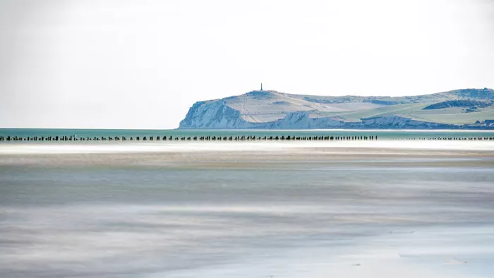 Kaap met kliffen in de verte achter een lage rij strandpalen en een licht, glad strand