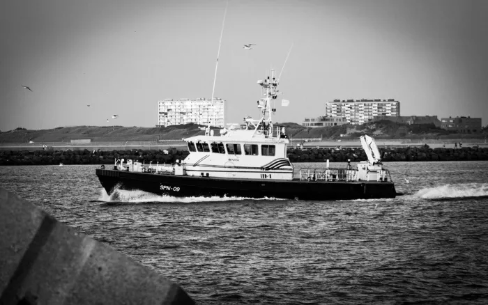 Patrouilleboot SPN-09 met witte boeggolf in de haven, met meeuwen en appartementsblokken op de achtergrond