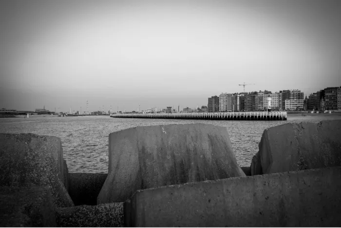 Betonnen golfbrekerblokken op de voorgrond met de pier en de skyline van Oostende in de verte