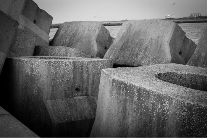 Opeengestapelde betonblokken van de golfbreker in Oostende, met hun ruwe textuur en schaduwen, en de zee en meeuwen op de achtergrond.