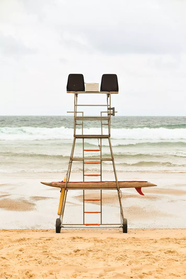 Hoge reddersstoel met twee zwarte zitjes en een surfplank op het strand voor de zee