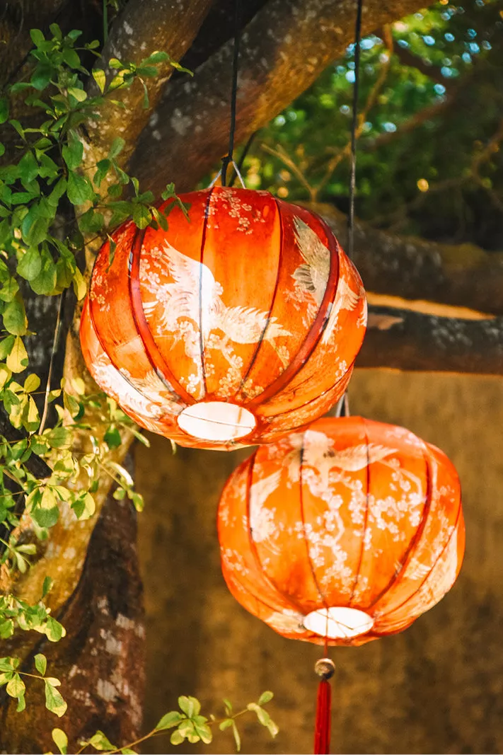 Twee oranje lampionnen met witte vlekken en een rode kwast in een boom