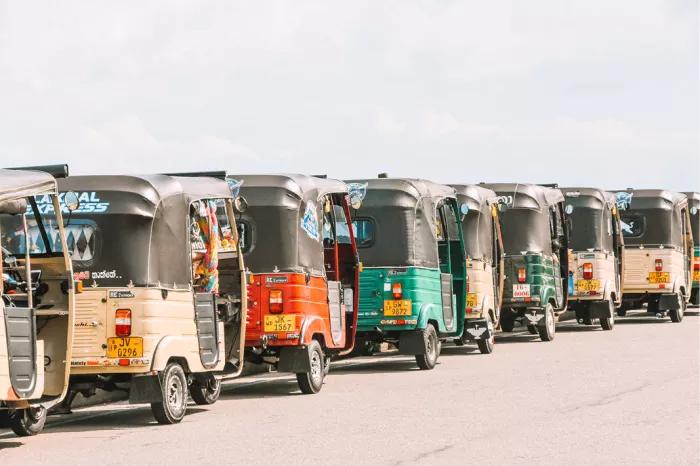 Lange rij kleurrijke tuktuks naast elkaar op een parkeerterrein onder een lichte lucht