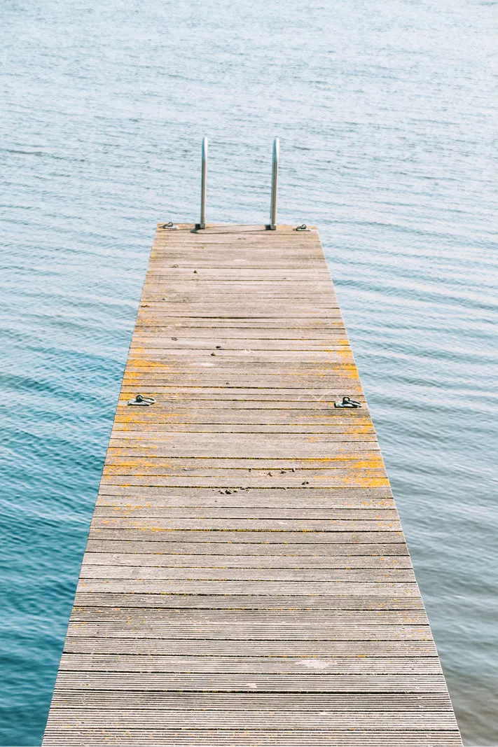 Houten steiger met een metalen trapje aan het einde, recht de blauwe zee in