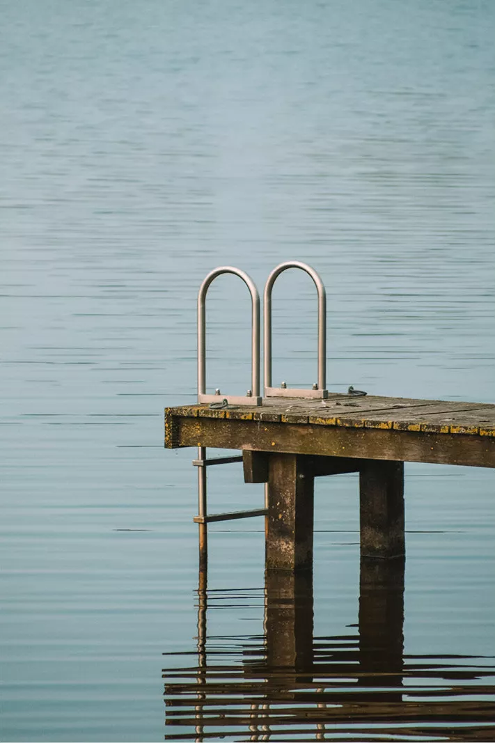 Klein houten steigertje met een metalen laddertje dat in rustig blauwgrijs water gaat