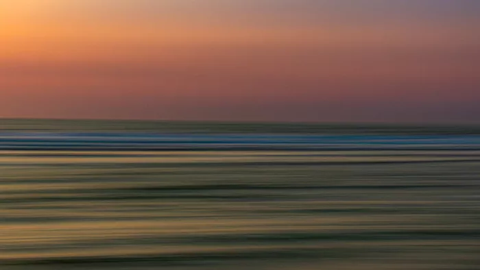 Abstract zeezicht met horizontaal uitgesmeerde banen water in olijfgroen en geel onder een gouden en bruine lucht.
