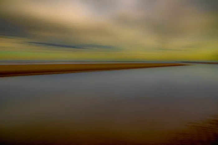Abstract kustlandschap met een zandbank en stil water onder een uitgeveegde, geelgroene lucht.