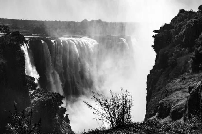 Waterval die in een kloof stort met opstijgende nevel tussen donkere begroeide rotswanden
