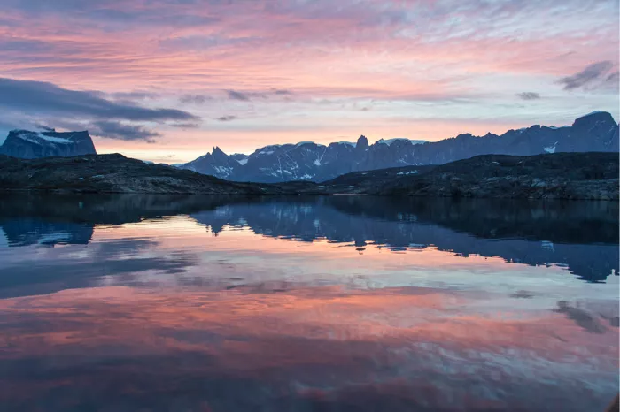 Roze en oranje avondlucht boven getande bergen die zich spiegelen in stil poolwater