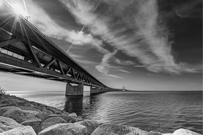 Öresundbrug strekt zich vanaf de rotsige oever tot ver over het water uit, met de zon die tussen de constructie door breekt.