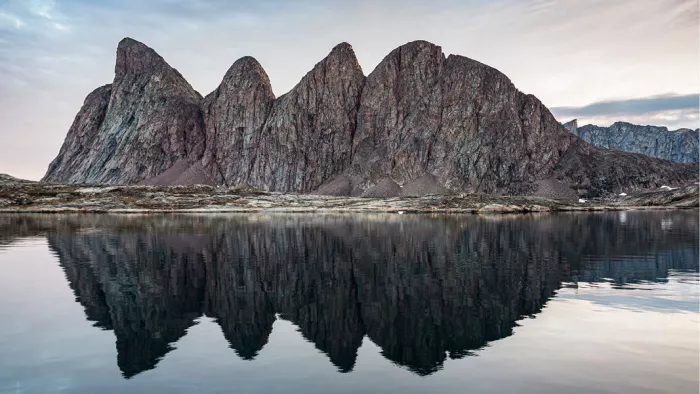 Getande roodbruine rotspieken die zich spiegelen in het stille water van een poolbaai