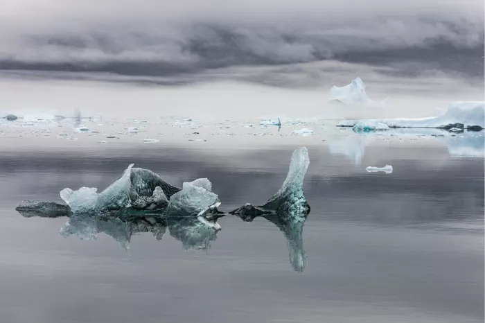 Kleine ijssculpturen en een rechtopstaande ijspilaar op spiegelglad water met ijsvelden erachter