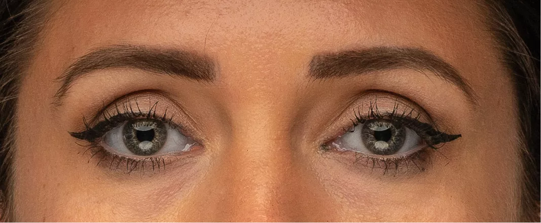 Close-up van twee vrouwenogen met grijsgroene irissen, zwarte eyeliner en wenkbrauwen
