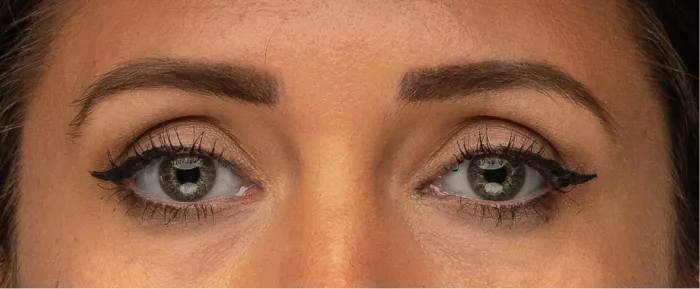 Close-up van twee vrouwenogen met grijsgroene irissen, zwarte eyeliner en wenkbrauwen