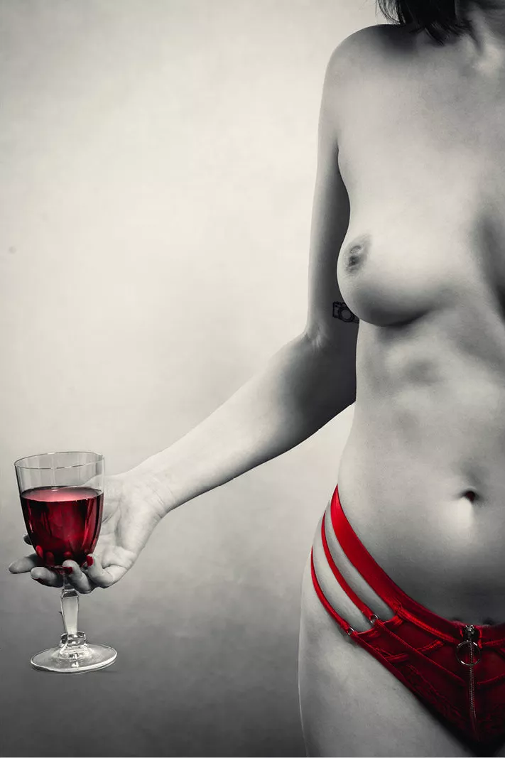 Vrouw in rode lingerie met uitgestrekte arm en een glas rode wijn, zwart-wit met rode accenten