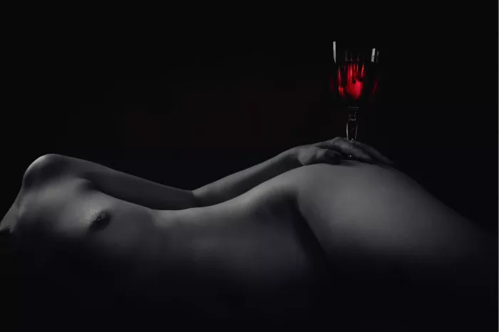 Liggende naakte vrouw met een glas rode wijn op de heup, zwart-wit met de wijn in rood